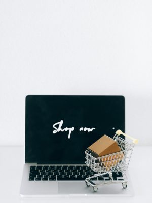A laptop screen displaying 'Shop now' with a miniature shopping cart and cardboard box.