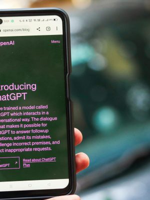 Close-up of a smartphone showing ChatGPT details on the OpenAI website, held by a person.