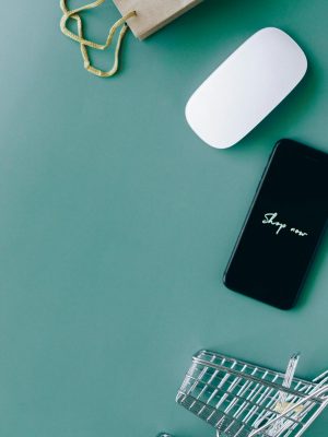 Flat lay of a smartphone, shopping cart, and paper bag representing online shopping and e-commerce.