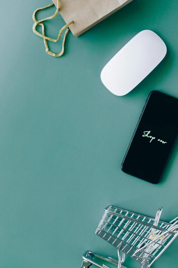 Flat lay of a smartphone, shopping cart, and paper bag representing online shopping and e-commerce.
